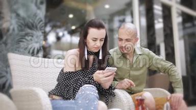 男人和女人在街头咖啡馆喝茶，看智能手机上的照片